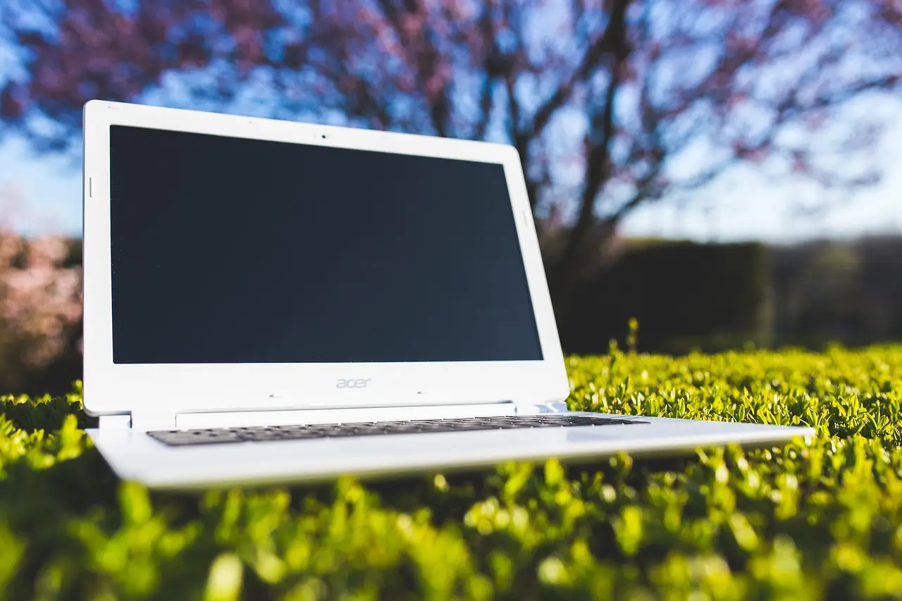 White laptop placed on green grass in sunlight